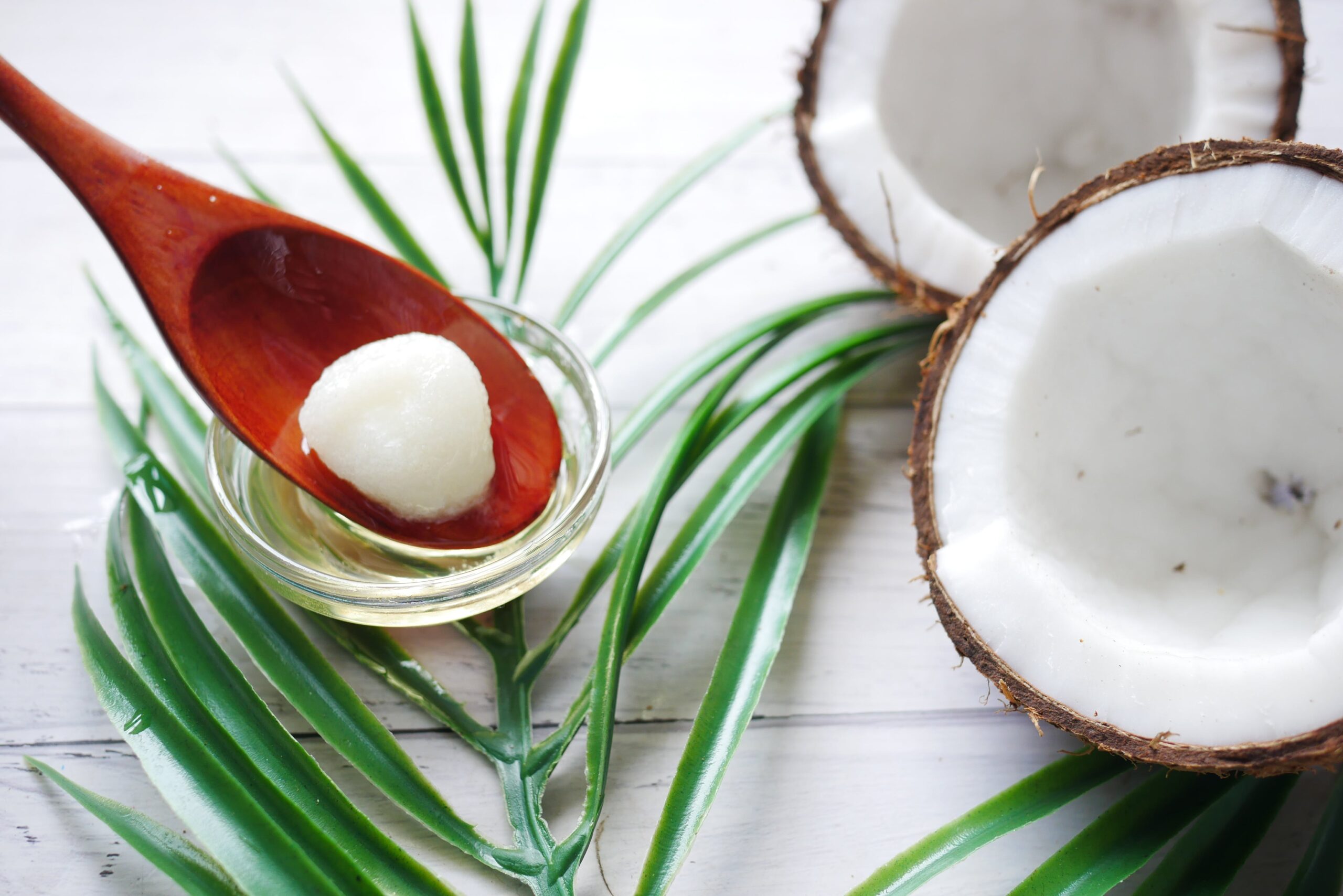 coconut oil on a wooden spoon next to coconuts