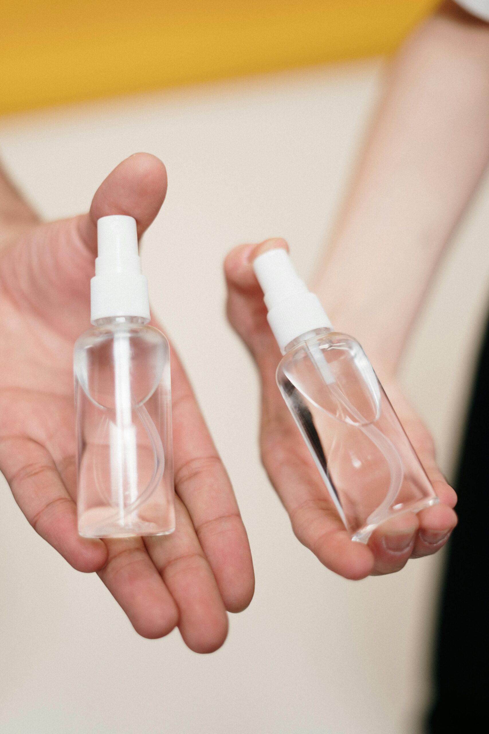 2 hands holding a glass spray bottle each