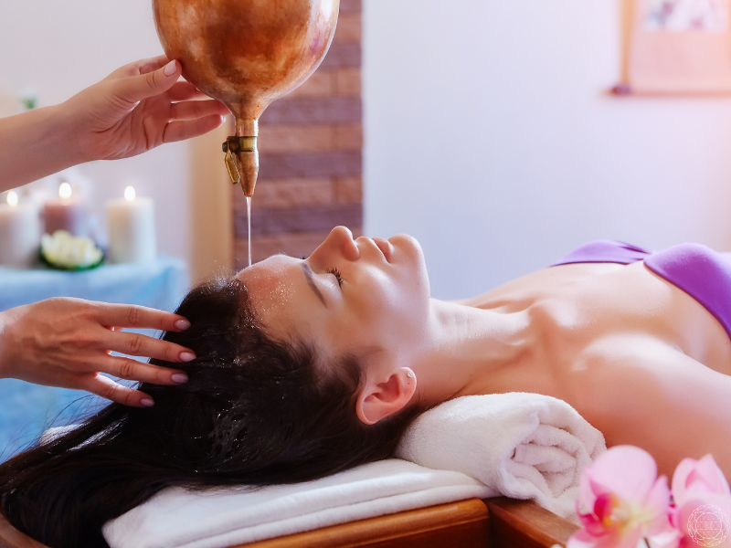 A peaceful Shirodhara scene with a woman in deep relaxation, surrounded by lit candles in the background.