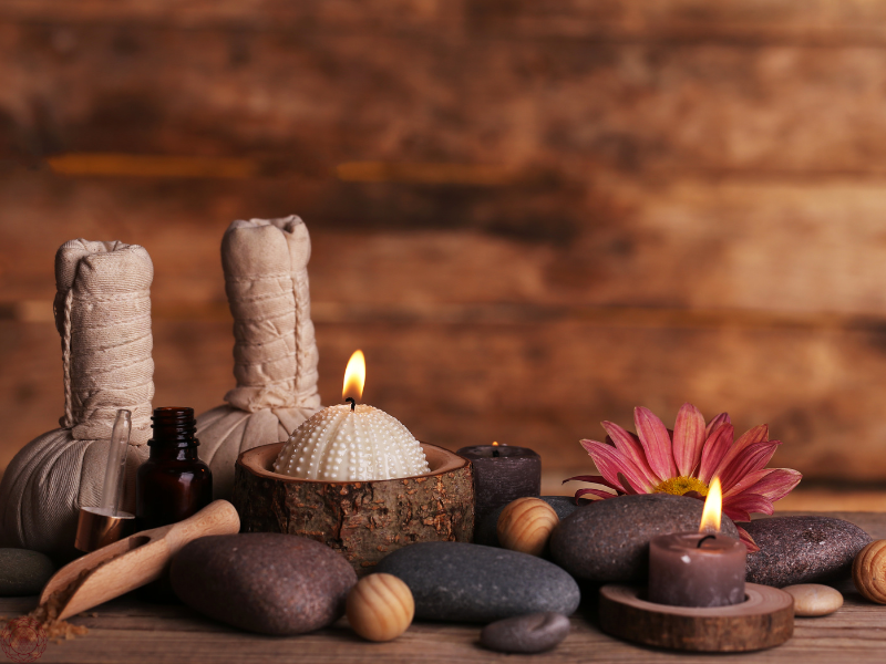 An arrangement of healing elements including smooth stones, miniature candles, a delicate flower, and a small tincture of herbal oil for Ayurvedic therapies.