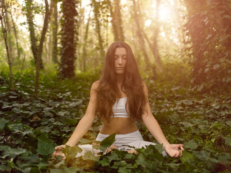 A serene woman with long brunette hair meditating peacefully in a forest, embodying the quiet introspection described in Autobiography of a Yogi.