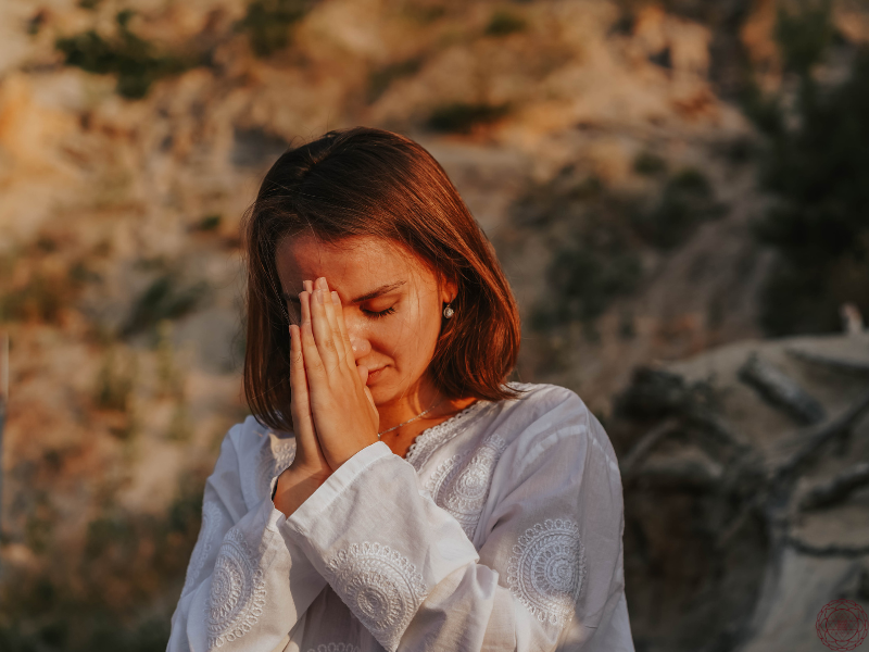 A woman in deep devotion with her hands in Anjali Mudra pressed to her forehead, eyes closed in reverence and prayer.
