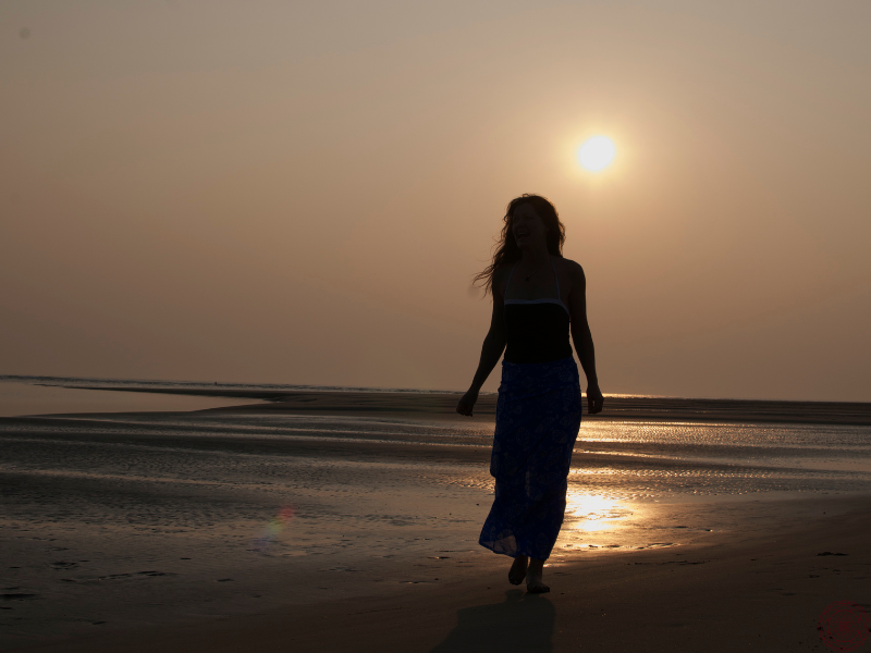 The silhouette of a woman walking along a beach at sunset, immersed in the sacred energy of light and movement.