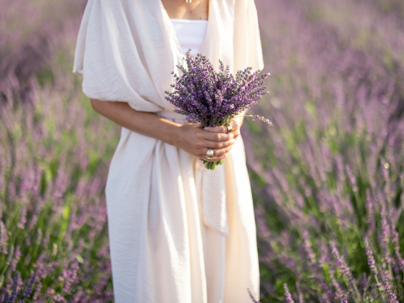 A woman in a flowing white gown holding lavender in a peaceful field, representing nurturing love and serenity.