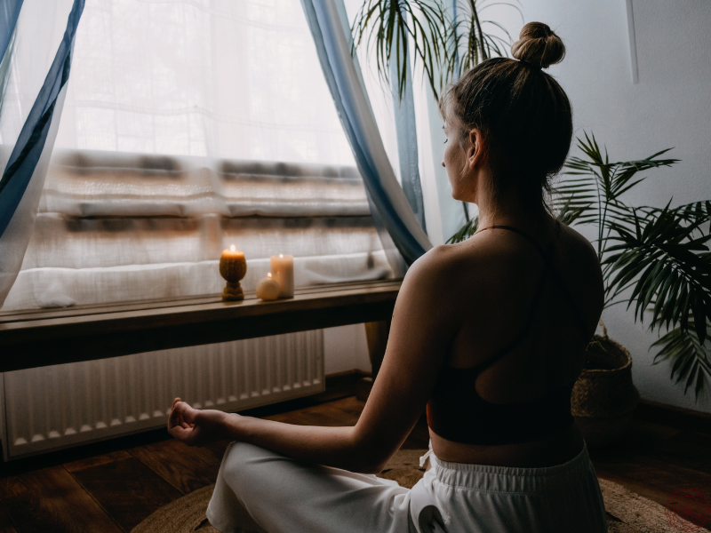 A woman sitting in meditation with two softly glowing candles in front of her, evoking a serene and sacred atmosphere.