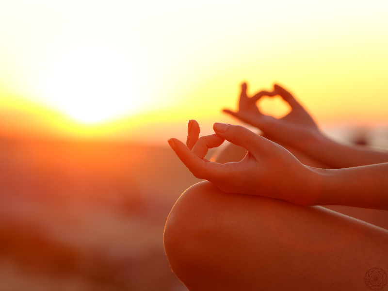 A serene close-up of hands in gyan mudra with a golden sunset in the background, representing Ayurveda’s grounding spiritual roots.