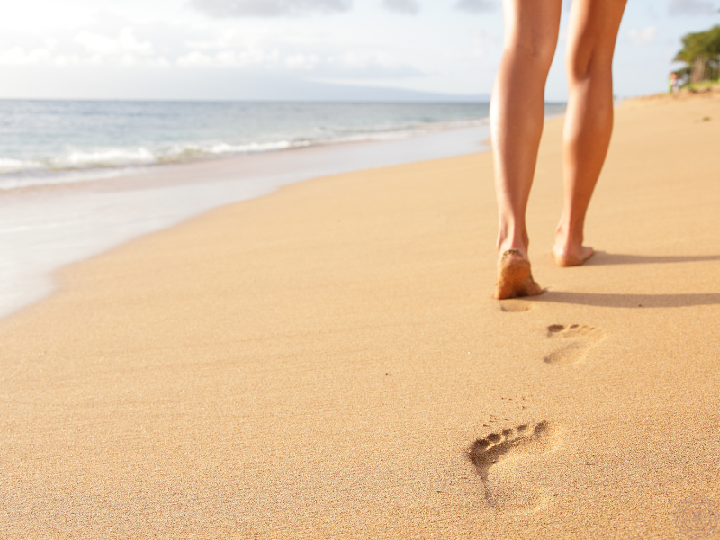 Legs walking on a beach with waves in the background, reflecting the soothing cardiovascular and meditative benefits of walking near water.