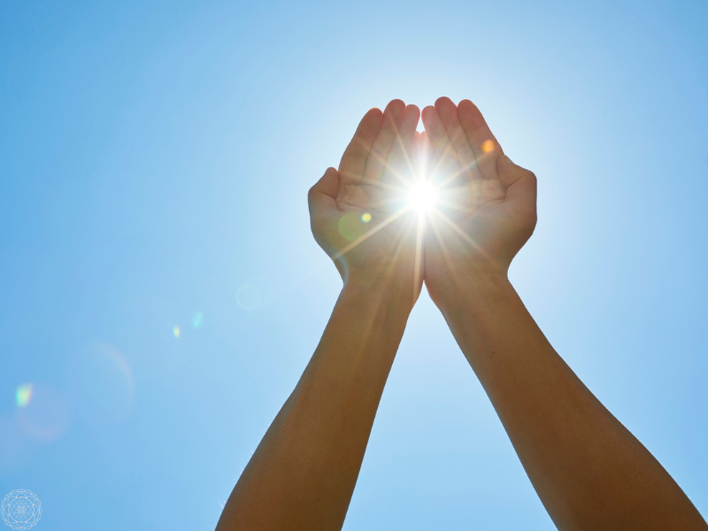 Hands gently cupping sunlight with a clear blue sky in the background, representing the act of receiving and channeling light codes.