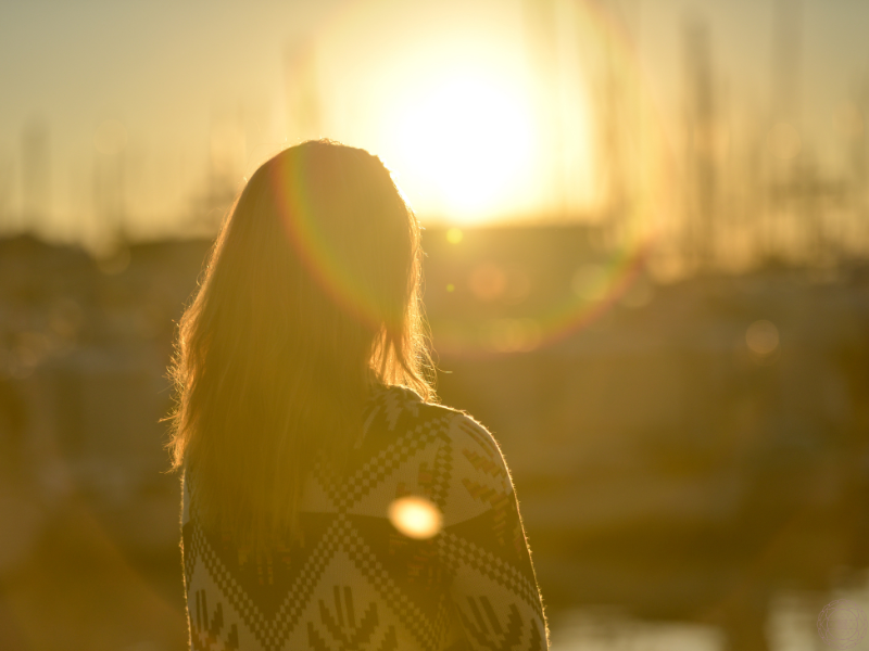 The back of a woman gazing at a vibrant setting sun, absorbing the luminous codes of transformation.