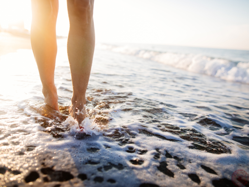 Bare legs standing in the ocean as the sun sets, symbolizing the calming and healing benefits of grounding with nature.