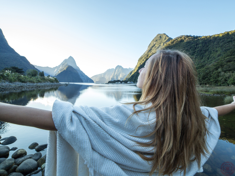 A woman with her arms spread wide, facing a river, symbolizing harmony with the Earth's natural frequencies and the power of the Schumann Resonance.