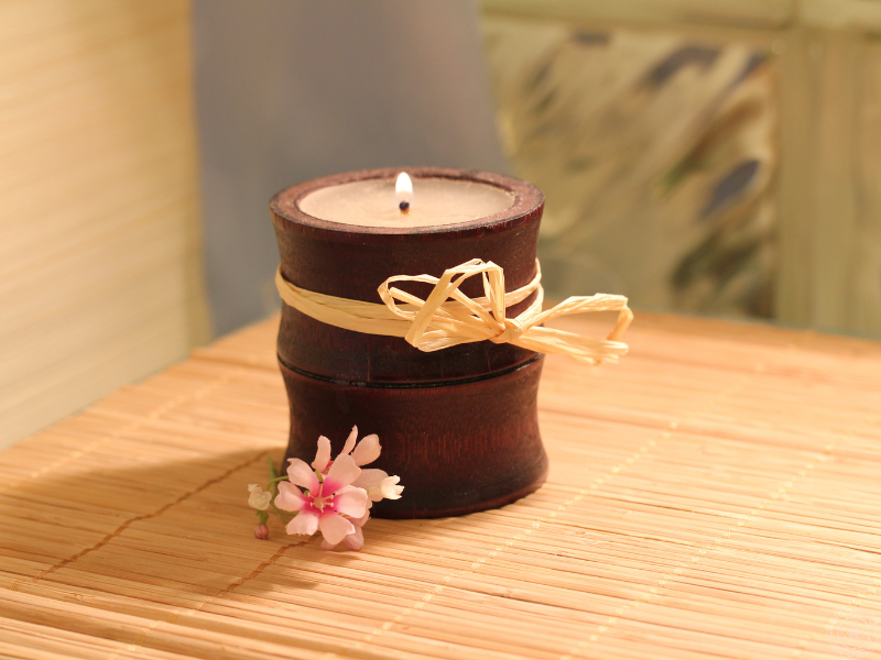 A softly lit candle on a bamboo mat with a delicate pink flower, representing calm, emotional healing, and sanctuary amidst fear.