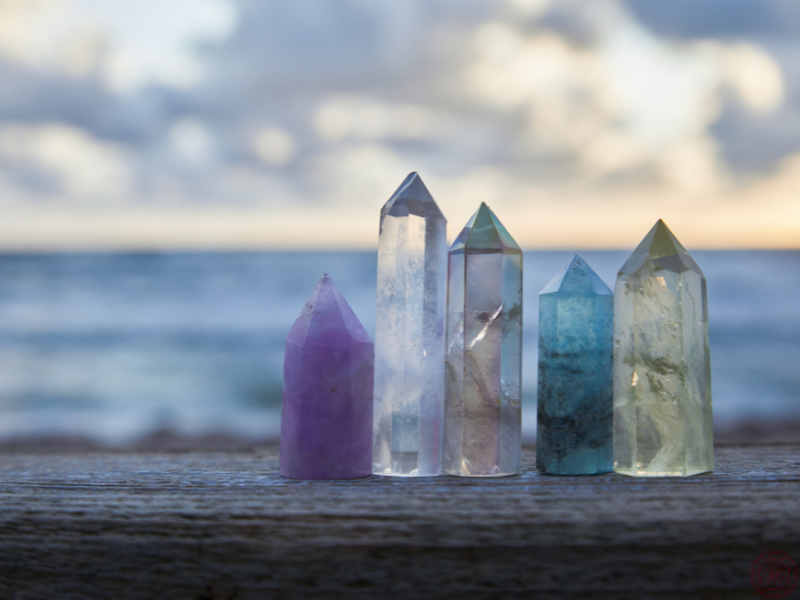 A selection of crystals placed on a wooden ledge with the ocean in the background, symbolizing chakra alignment and energy balance through the use of healing stones.