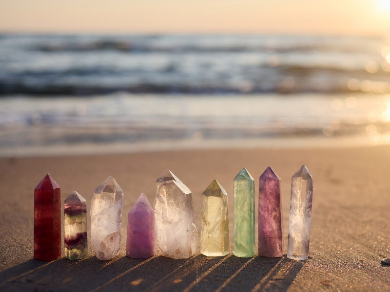 A variety of colorful crystals arranged on a beach, symbolizing the energetic centers of the body known as chakras and their connection to the natural elements.