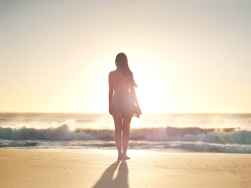 A woman standing at the edge of the ocean, gazing into the sunset, symbolizing contemplation of one’s life path and higher purpose- core elements of discovering dharma.