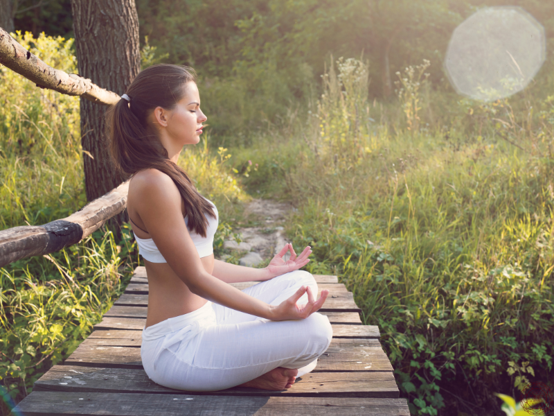 A woman meditating outdoors in a white yoga set, embodying stillness, mindfulness, and the inner calm cultivated through pranayama techniques.