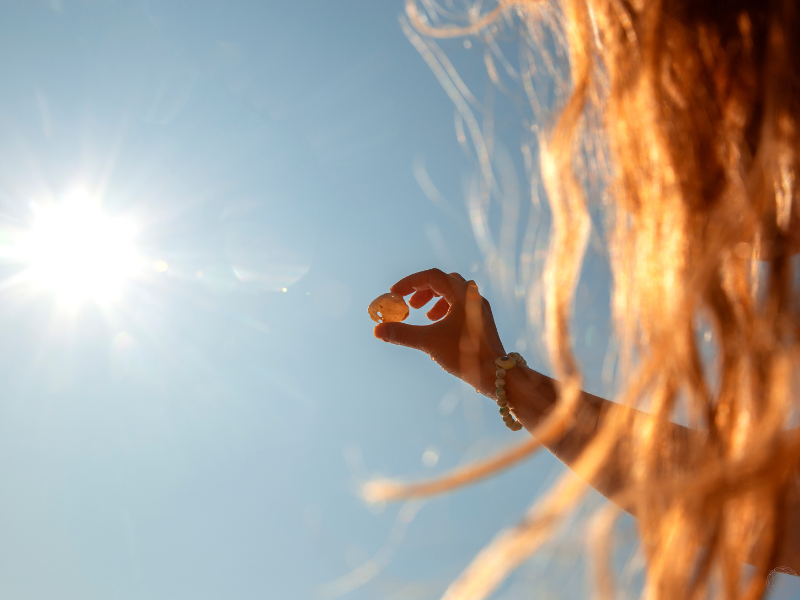 A woman holding an orange crystal up to the sky as sunlight streams through, suggesting the search for clarity and Truth through spiritual insight.