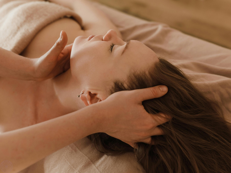 A woman lying down with eyes closed, receiving a head massage, representing the doorway of touch and its calming influence on the mind.
