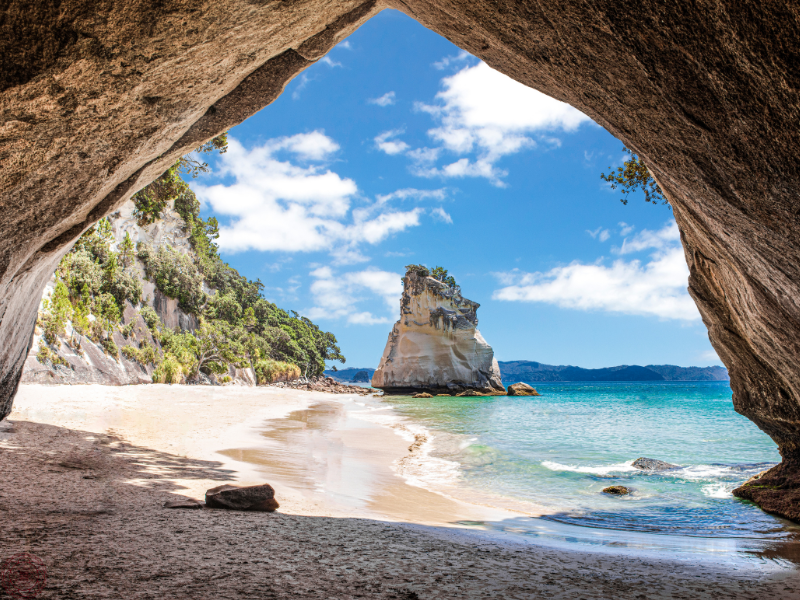 The view from inside a rocky cove looking out at a sunlit beach, suggesting the perspective shift that comes from slowing down.