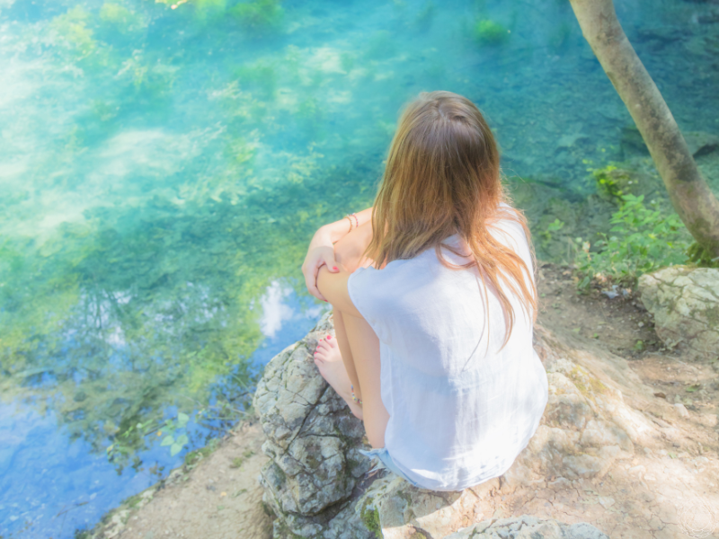 A woman sitting on a rock overlooking vibrant blue water, lost in thought as she gazes at the vast horizon.