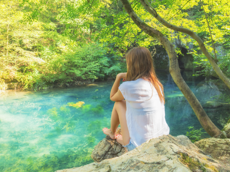 A woman sitting on a rock overlooking vibrant blue water, embodying quiet reflection and stillness.