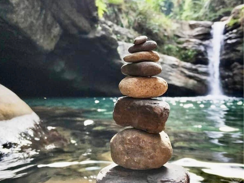 A stack of balanced rocks in front of a waterfall, symbolizing harmony, stillness, and the balance found in letting go.