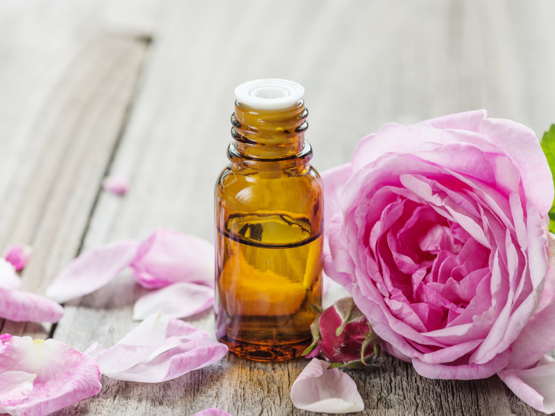 A close-up of an essential oil bottle with a soft pink rose beside it, symbolizing emotional healing and calm.