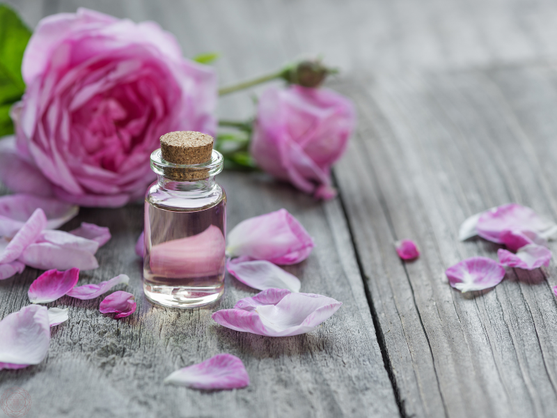 A small essential oil bottle with a pink rose in the background, representing gentle floral aromatherapy for mood support.