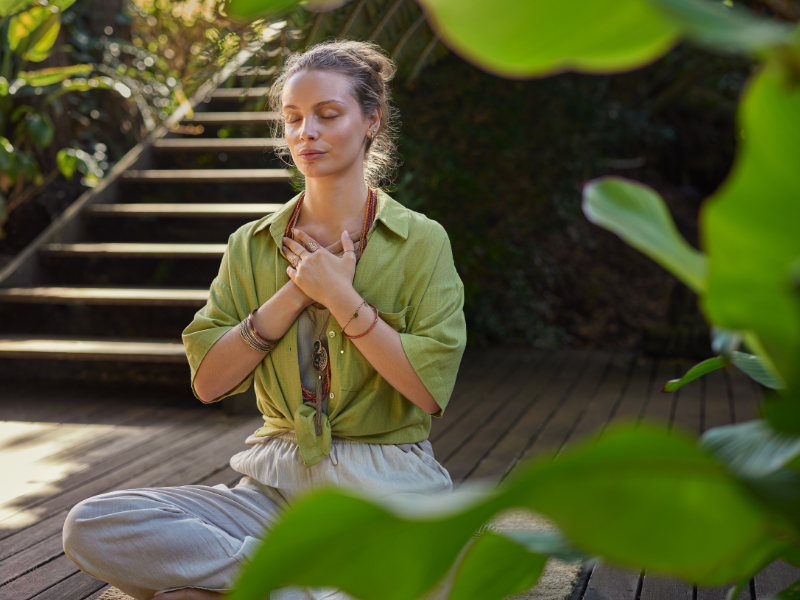 Woman sitting in meditation outdoors with hands over her heart, embodying presence and spiritual awakening.