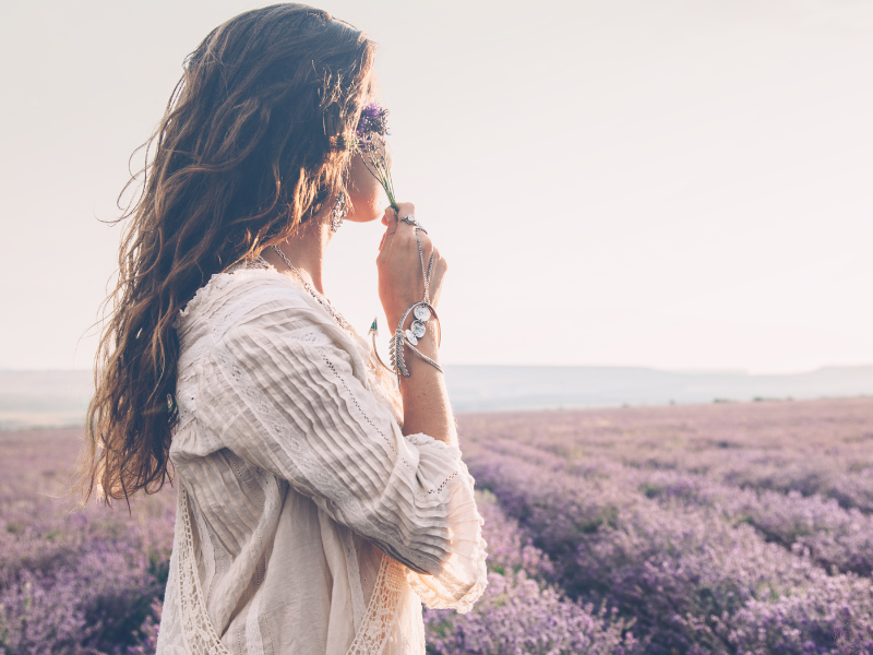 Woman standing angelically in a field of purple flowers, representing Divine connection and the presence of A Course in Miracles.