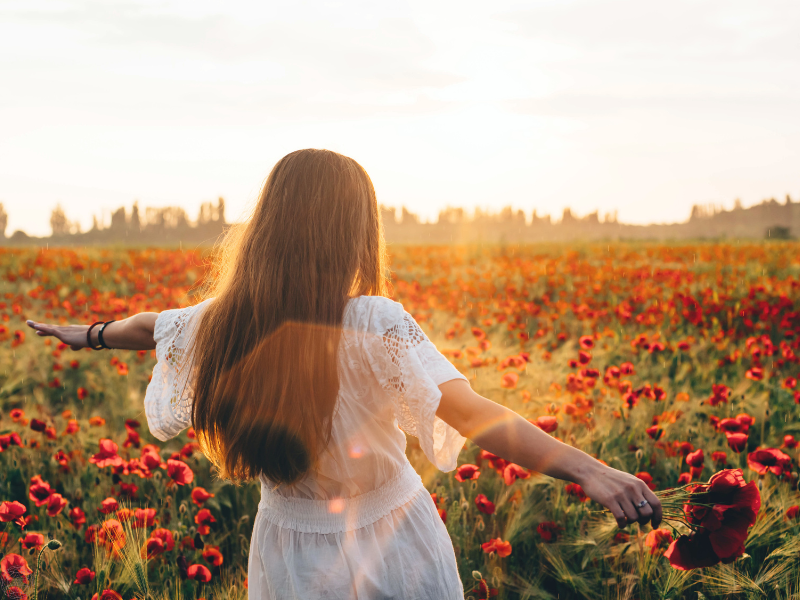 Woman in a white dress joyfully moving through a flower field, reflecting freedom and alignment with her north star.