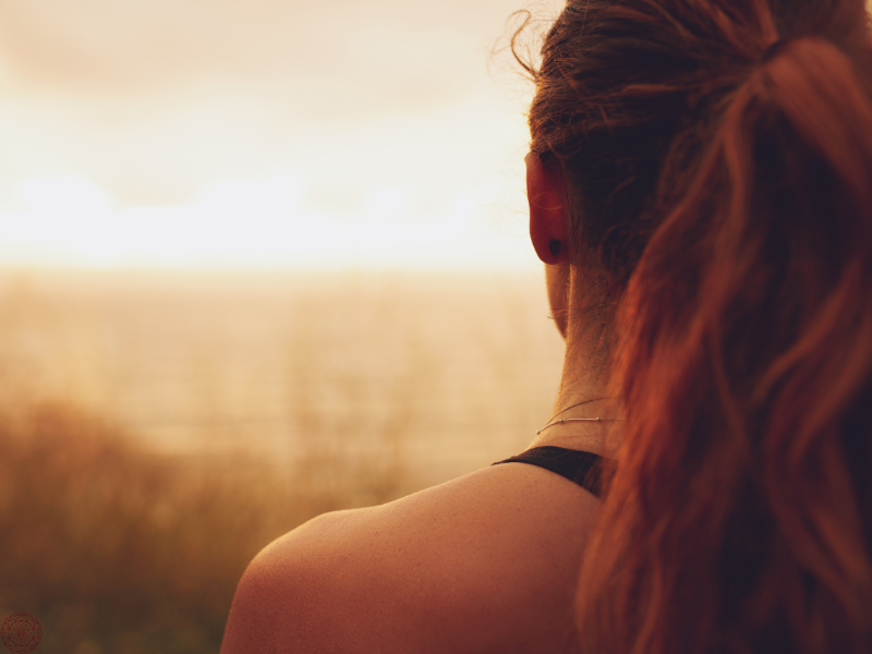 Back of a woman gazing at a setting sun, reflecting the introspective path of a starseed.
