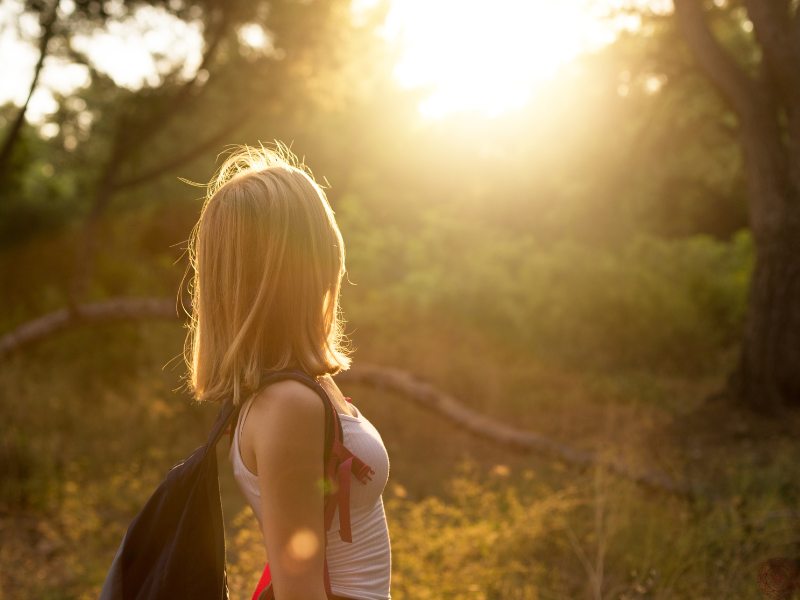 Woman in a forest gazing at the sun, embodying the connection between starseeds and nature.