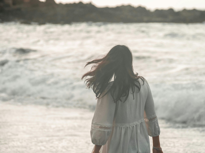 Back of a woman wearing a white dress gazing at the ocean, evoking serenity and the freedom that comes after shadow integration.