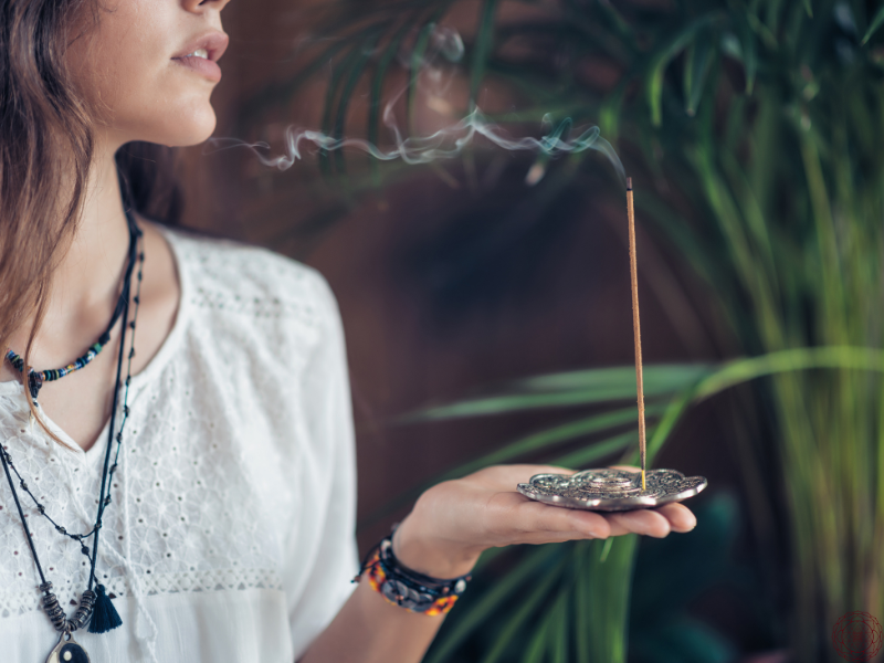 Close up of a woman holding a burning stick of incense, symbolizing inner cleansing and reflection through shadow work.
