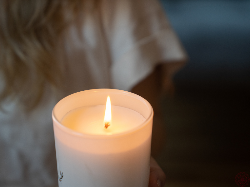 Close up of a woman holding a lit candle in a dim room, representing awareness and illumination of the shadow self.