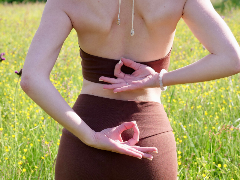 Woman out in nature with her hands behind her back in gyan mudra, representing wisdom, calm, and spiritual focus.