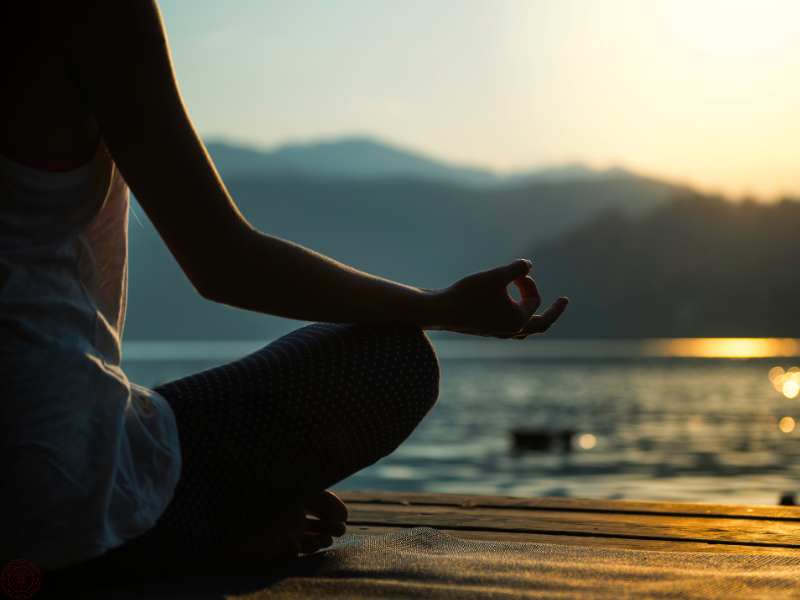 Close up of a woman meditating on the dock of a lake at sunset, symbolizing peace and introspection.