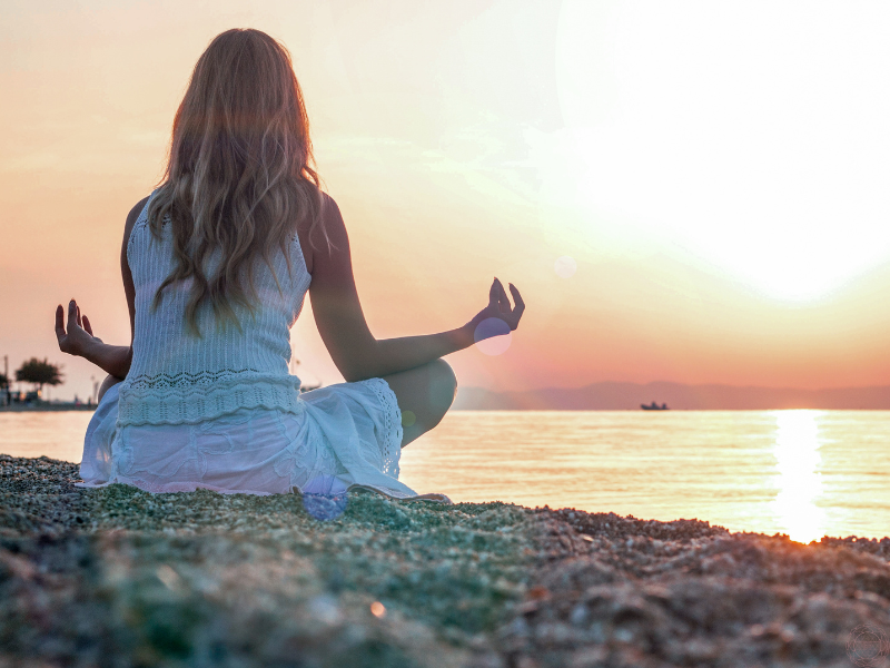 Back view of a woman meditating in nature, symbolizing the layers of the self explored in the three bodies and five koshas.