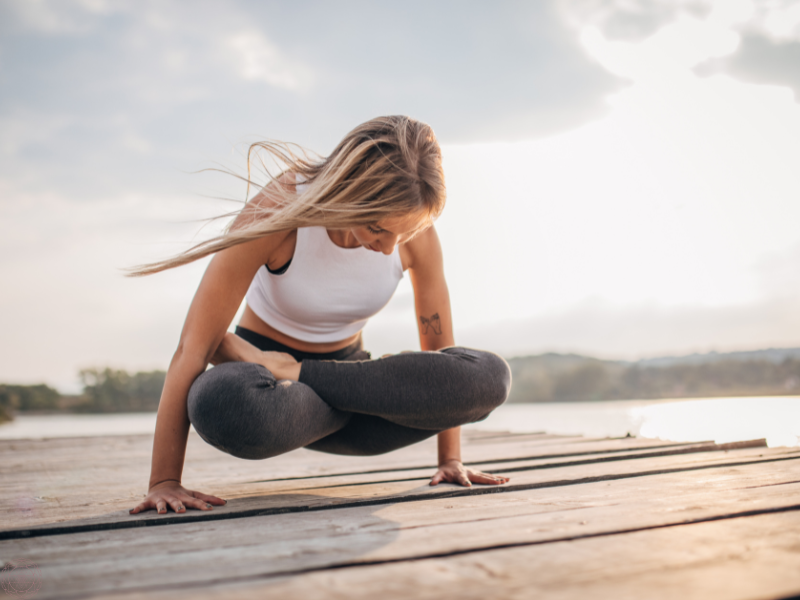 A woman practicing yoga on a dock overlooking the water, symbolizing harmony between the physical body and subtle energy layers.