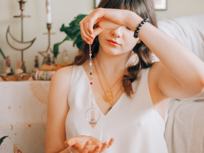 Woman holding a multicolored crystal pendulum, symbolizing conscious awareness of energetic shifts and life’s changing polarities.
